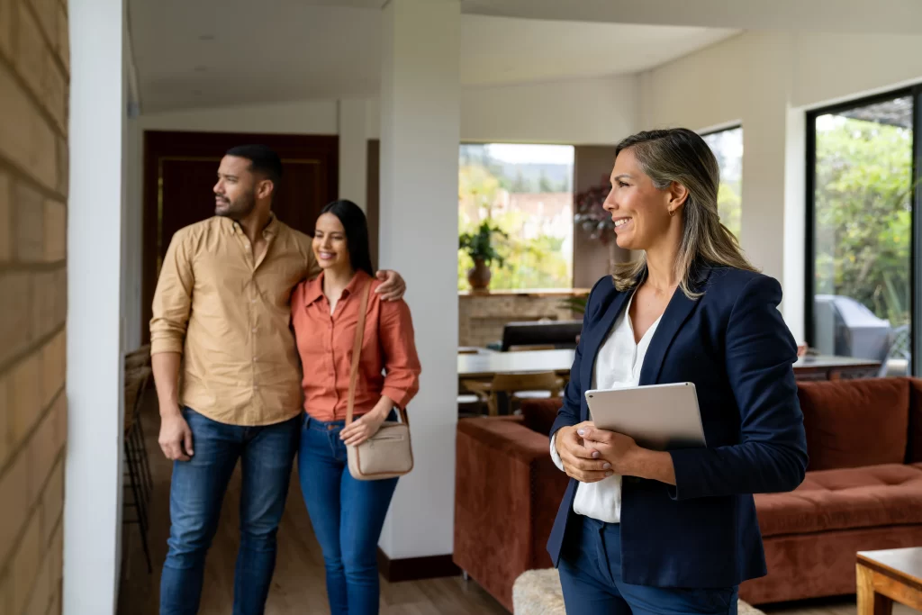 Real estate agent holding a tablet while a couple tours a bright, modern home.